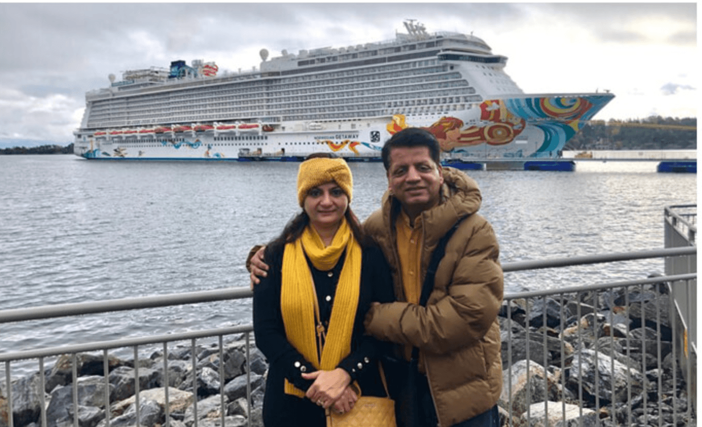 Two travellers wrapped up against the cold at a harbour, a vast cruise ship moored on the water behind them.